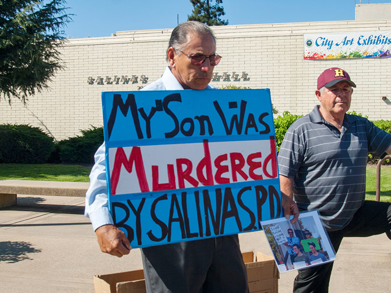Frank Alvarado Sr. holds a sign on October 1, 2014 in front of Salinas City Hall reading, "My Son Was Murdered By Salinas PD." Frank Alvarado Sr. is also displaying a photo of his son, Frank Alvarado, who is holding a sign on May 14, 2014 stating “Invest in Protecting and Healing, Not in Caging” before speaking at a Sin Barras rally at the Santa Cruz Courthouse for building strong communities in California, not more jails!