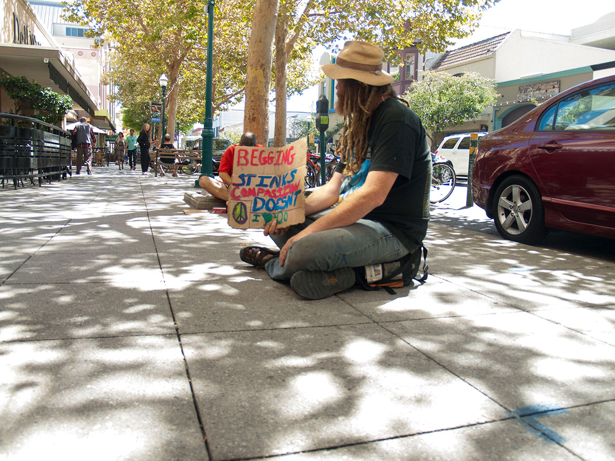 Druid sits while holding a sign near Santa Cruz Coffee Roasting Company on Pacific Avenue, “Begging Stinks. Compassion Doesn’t. I (heart) 420”